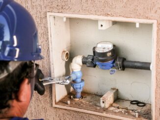 Instalador verificando medidor de água em painel externo de parede, foco em manutenção e controle de consumo hidráulico, essencial para gestão eficiente de recursos ambientais.