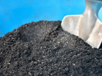 Carvão vegetal preto em uma superfície com uma pá de jardim ao lado, utilizado na agricultura, na produção de energia ou na indústria de alimentos, representando práticas sustentáveis e economia de recursos naturais.