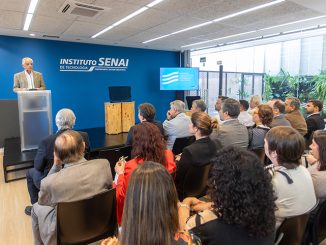Palestrante apresentando em evento do Instituto SENAI com audiência de profissionais em ambiente moderno de sala de conferências.