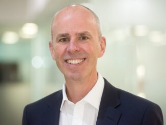 Homem de negócios sorridente em ambiente corporativo, usando terno preto e camisa branca. Fotografia profissional voltada para temas de sustentabilidade e mercado ambiental.