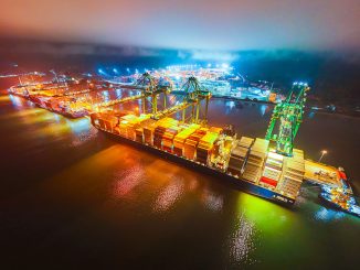 Contêineres de transporte marítimo iluminados à noite, movimentação portuária, logística e comércio internacional, representando a dinâmica do setor de transporte de cargas.