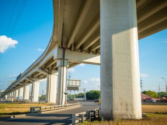 Elevada ferrovia de concreto sob céu azul claro, infraestrutura de transporte urbano, moderna e sustentável, vista de baixo, com postes de energia elétrica ao fundo.