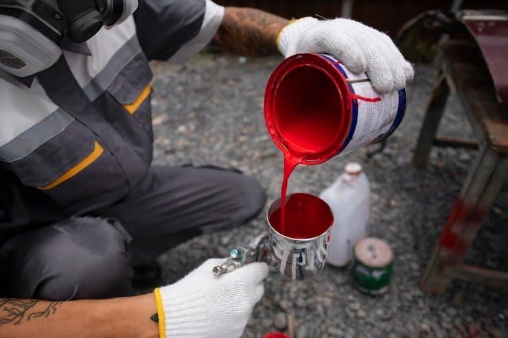 Person pouring red paint into a can for interior painting project.