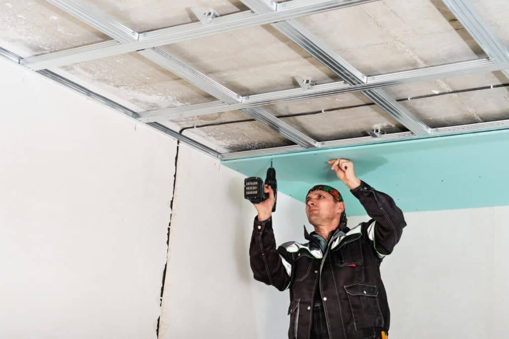Worker removing popcorn ceiling with drill in renovation project.