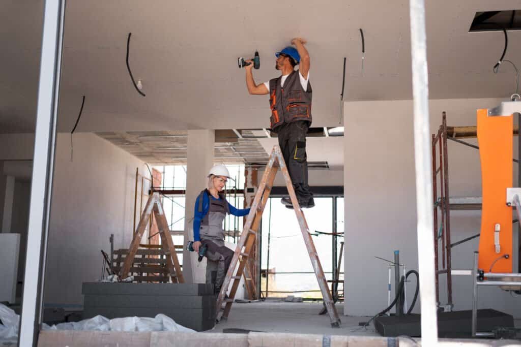 Workers renovating interior ceiling with power tools and ladders.