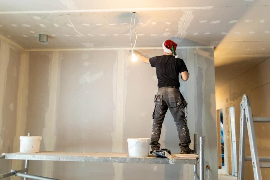 Painter working on drywall with Christmas hat in renovation project.