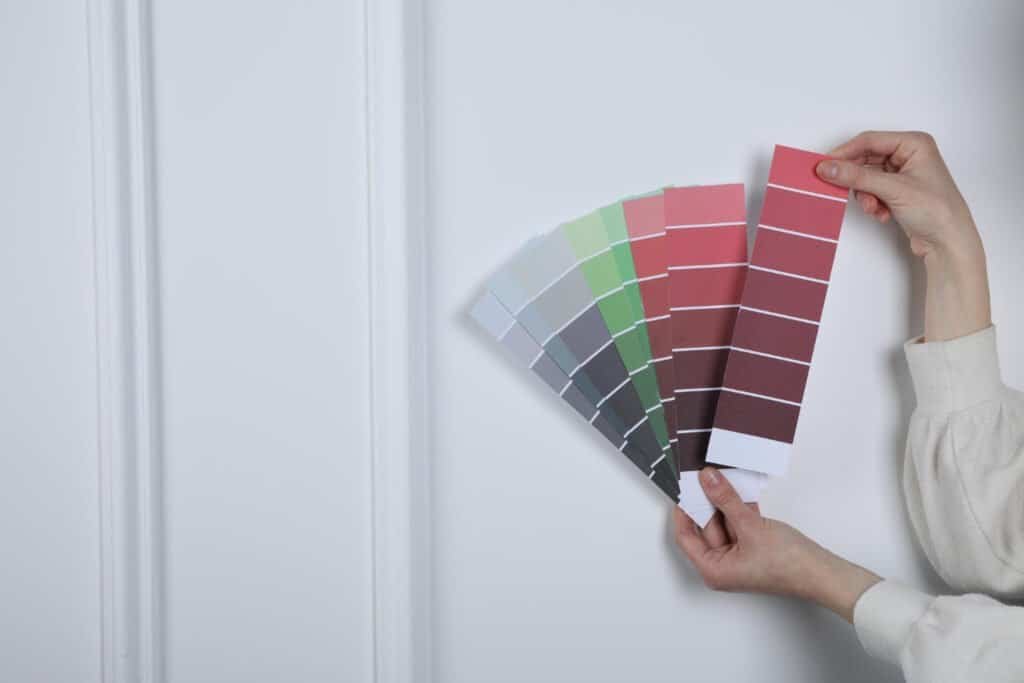 Person holding paint color swatches for interior wall painting.