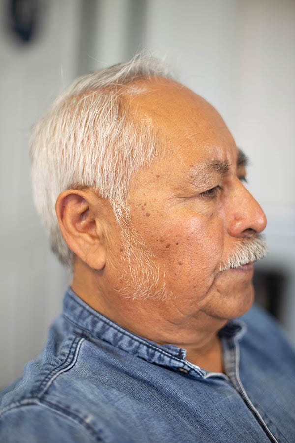 A side view of an older man that has white hair, with a comb-over haircut. long side burns and a mustache.