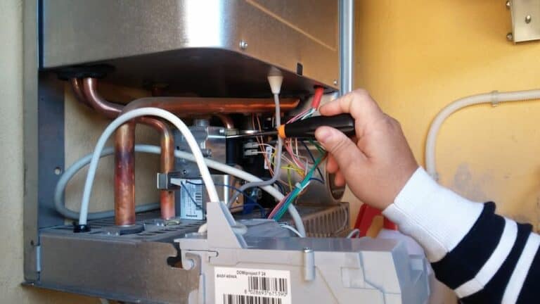 A person uses a tool to work on the wiring and pipes inside an open wall-mounted electrical or gas unit during an oil to gas conversion.