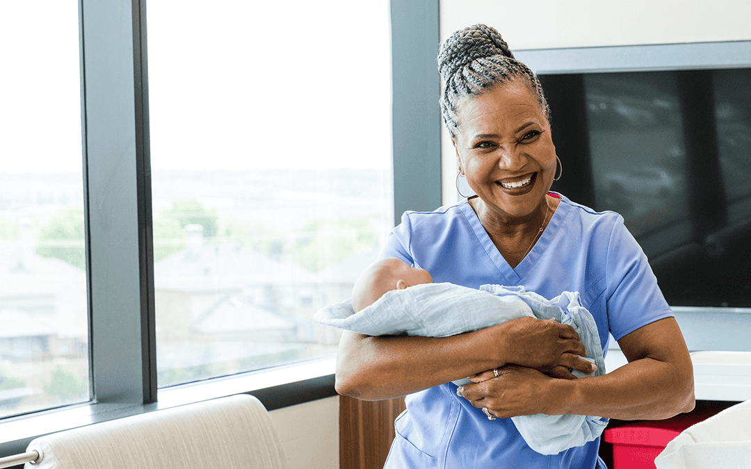 A midwife holding a newborn baby and smiling.
