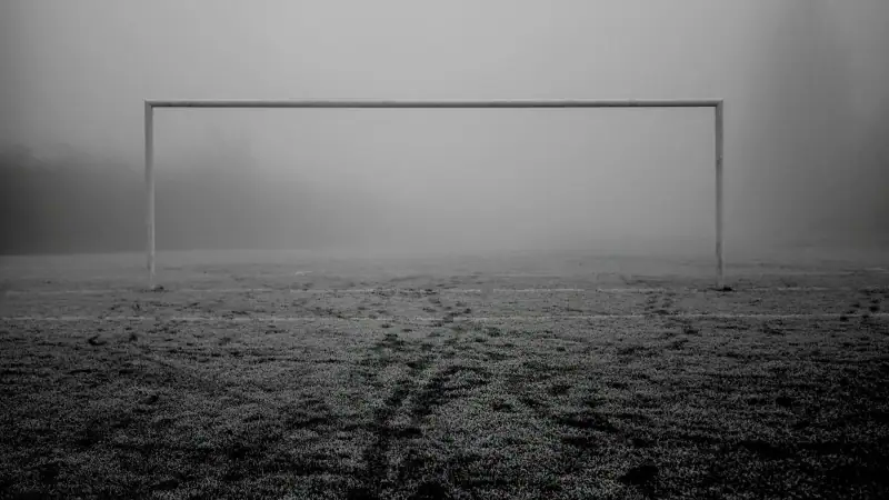 Black and white photo of a soccer goalpost on a frosty, foggy pitch.