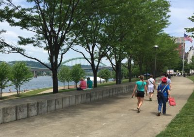 Scenic riverside trail with people walking and relaxing under trees.