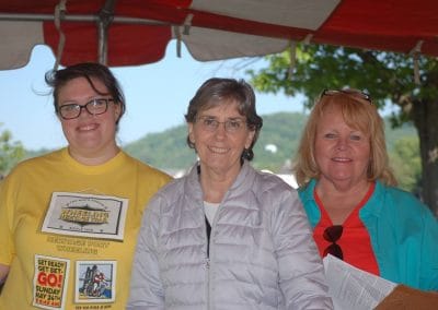 Group of three women smiling at an outdoor event under a red canopy.