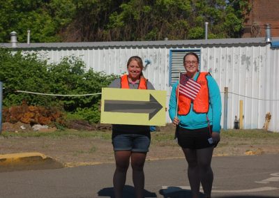Two women holding a directional arrow sign on a trail.
