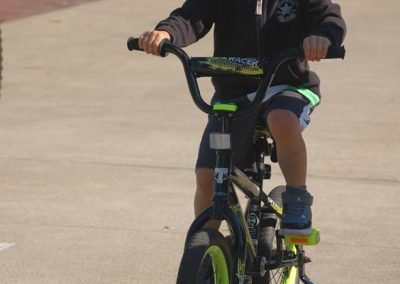 Young boy riding a bike with training wheels on a paved trail.