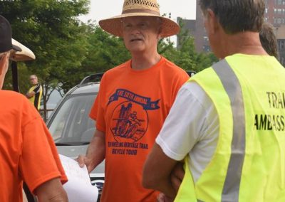 Trail event organizer in orange shirt and straw hat talking with volunteers.
