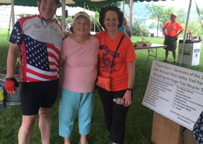 A group of three smiling people standing under a tent at an outdoor event.