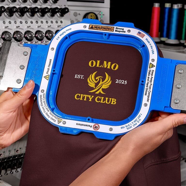 Écusson brodé OLMO CITY CLUB sur sweat à capuche, symbole d'élégance et de style urbain.