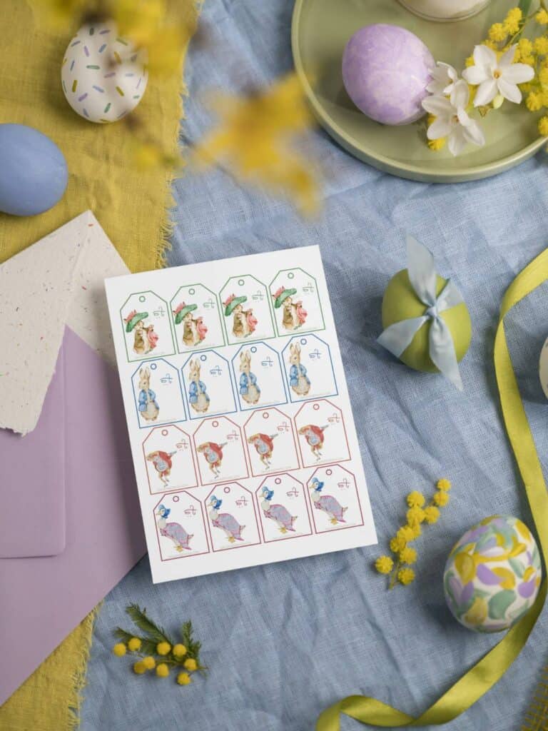 Peter Rabbit and Friends Easter "To" gift tags on a sheet laying on colorful tablecloth with eggs and flowers.