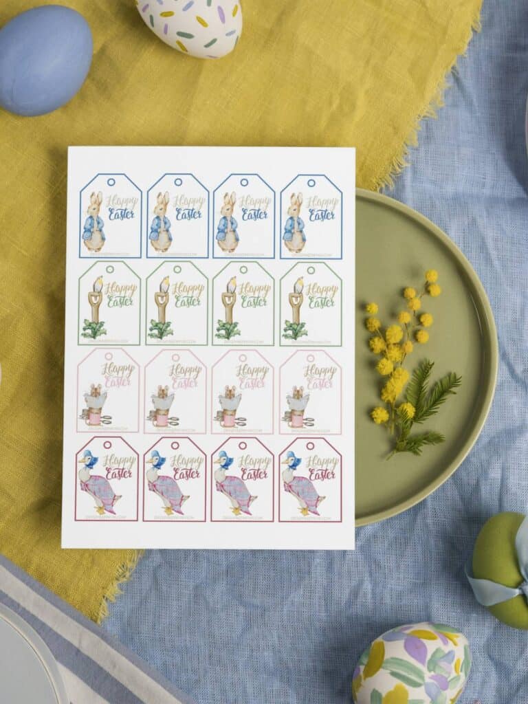 Peter Rabbit and Friends Happy Easter gift tags in a sheet laying on pastel tablecloth in yellow and blue and a plate with flowers.