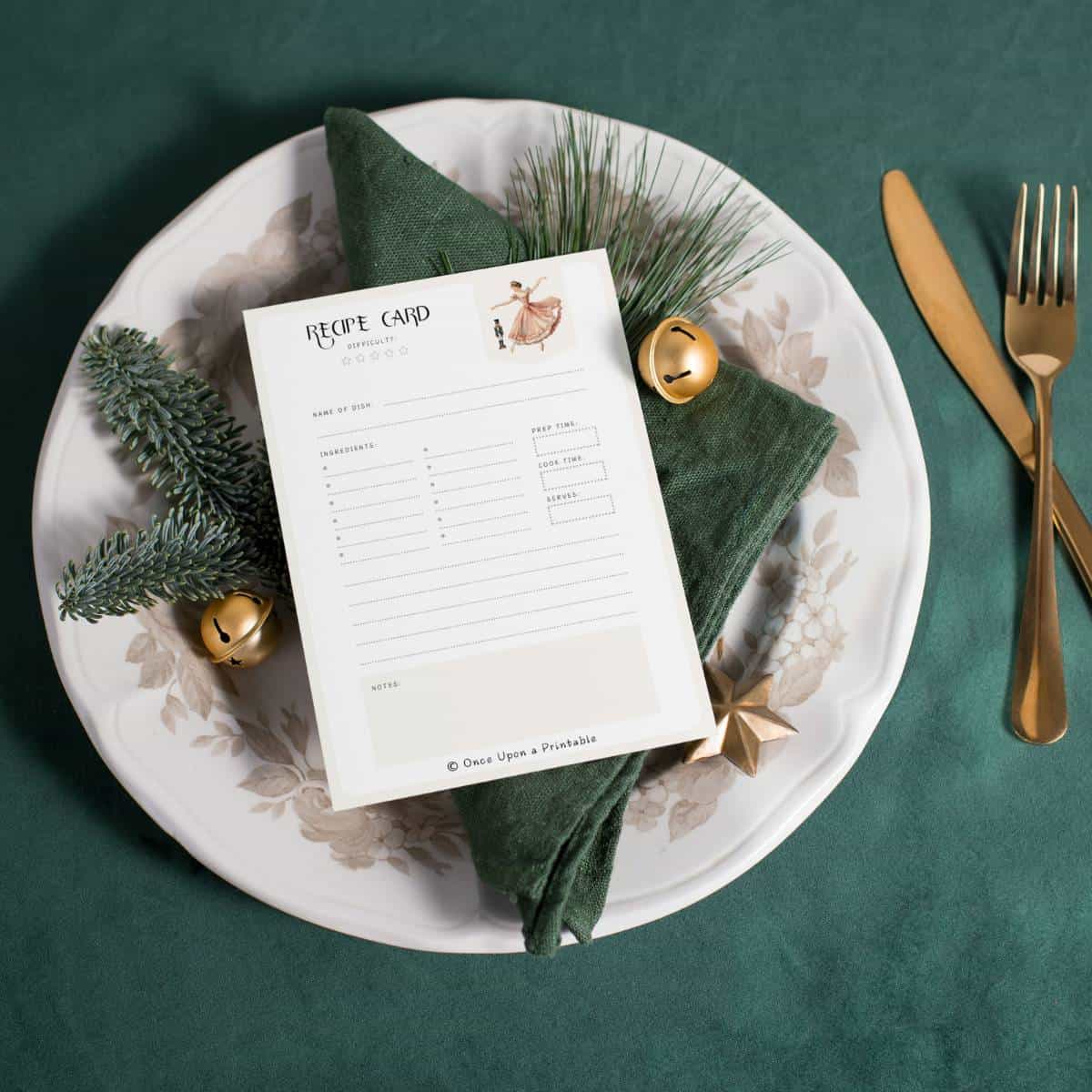 Nutcracker-themed Maria and the Nutcracker recipe card sitting on a green napkin, garland, and white plate on a green velvet tablecloth.