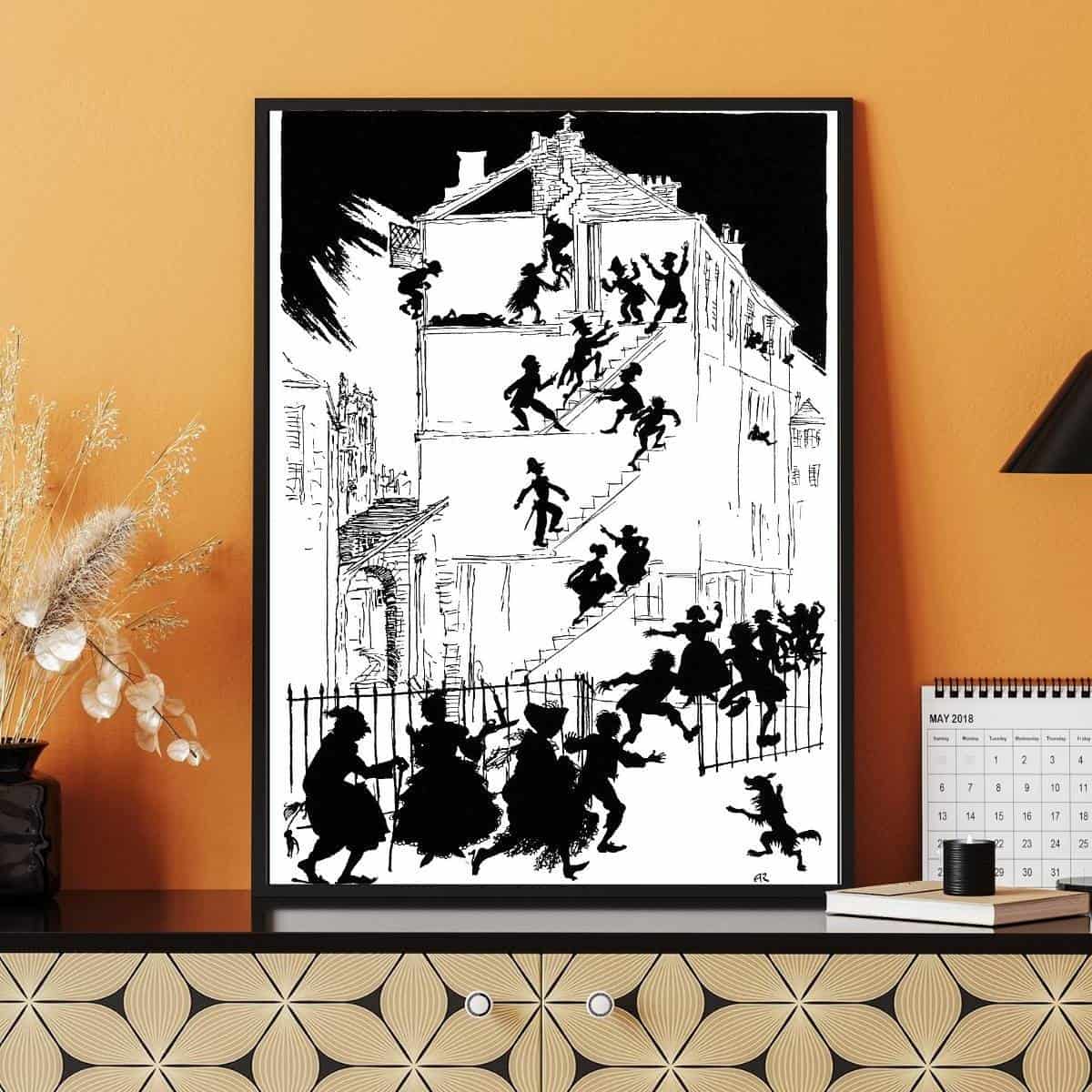 A black and white house full of characters, an illustration from Arthur Rackham framed displayed on a modern desk up against an orange wall.