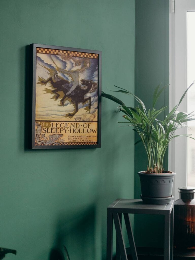 The legend of Sleepy Hollow illustrations by Arthur Rackham framed and displayed on a green wall next to a table and potted plant.