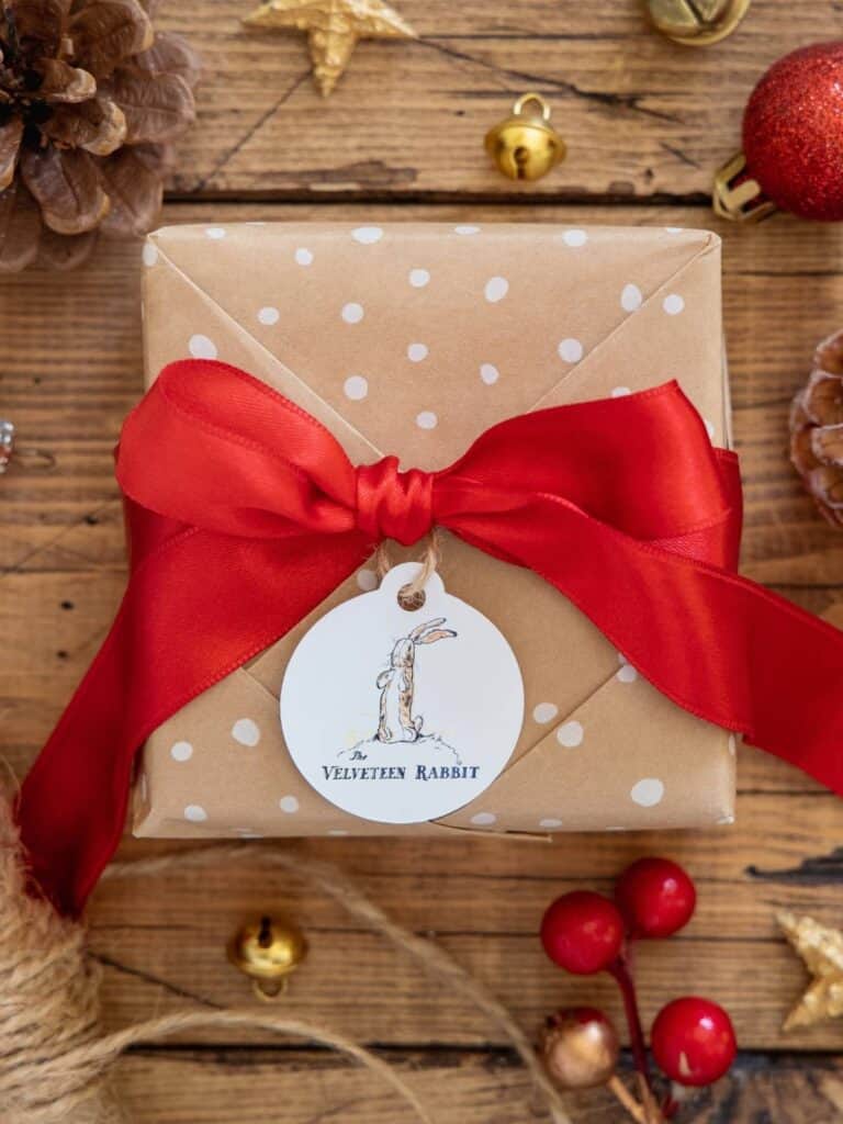 The Velveteen Rabbit gift tags on a brown paper package tied with a big satin red ribbon, pinecones, and red berries.