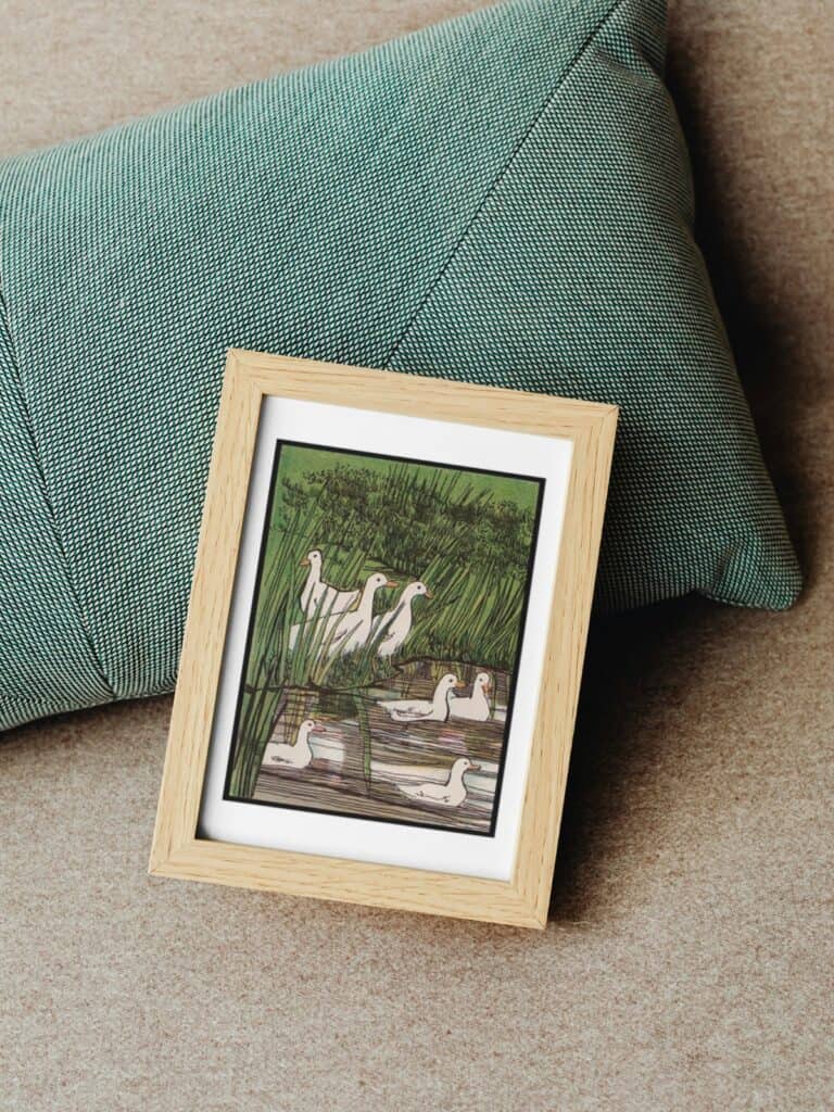 Vintage illustration of ducks in a stream framed and sitting on a green pillow.