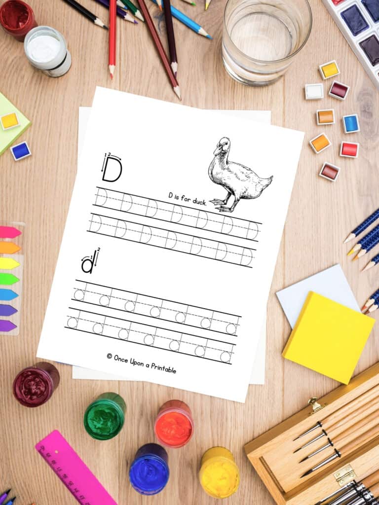 Letter D is for Duck letter practice uppercase and lowercase laying on a wooden table with coloring supplies.