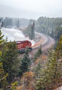 Red Canadian Pacific train on curved snow-covered tracks beside a frozen river and forest.