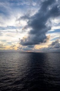 Ocean view at sunset with dark clouds and a distant city skyline on the horizon.