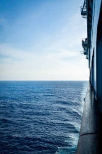 Ocean view from the side of a large vessel with railing and ship structure visible on the right.
