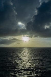 Ocean view with dark clouds and sunlight reflecting on the water surface.