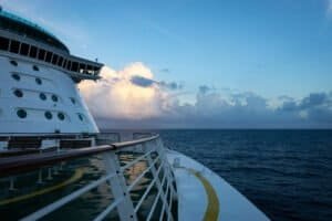 View from a cruise ship deck showing railing, benches, ocean, and partly cloudy sky.