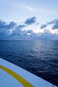 Ocean view under cloudy sky, seen from edge of white structure with yellow stripe.