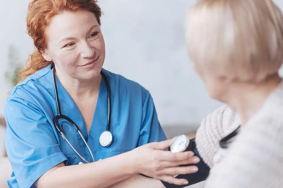 A nurse in blue scrubs checks the blood pressure of an older woman during a medical appointment.