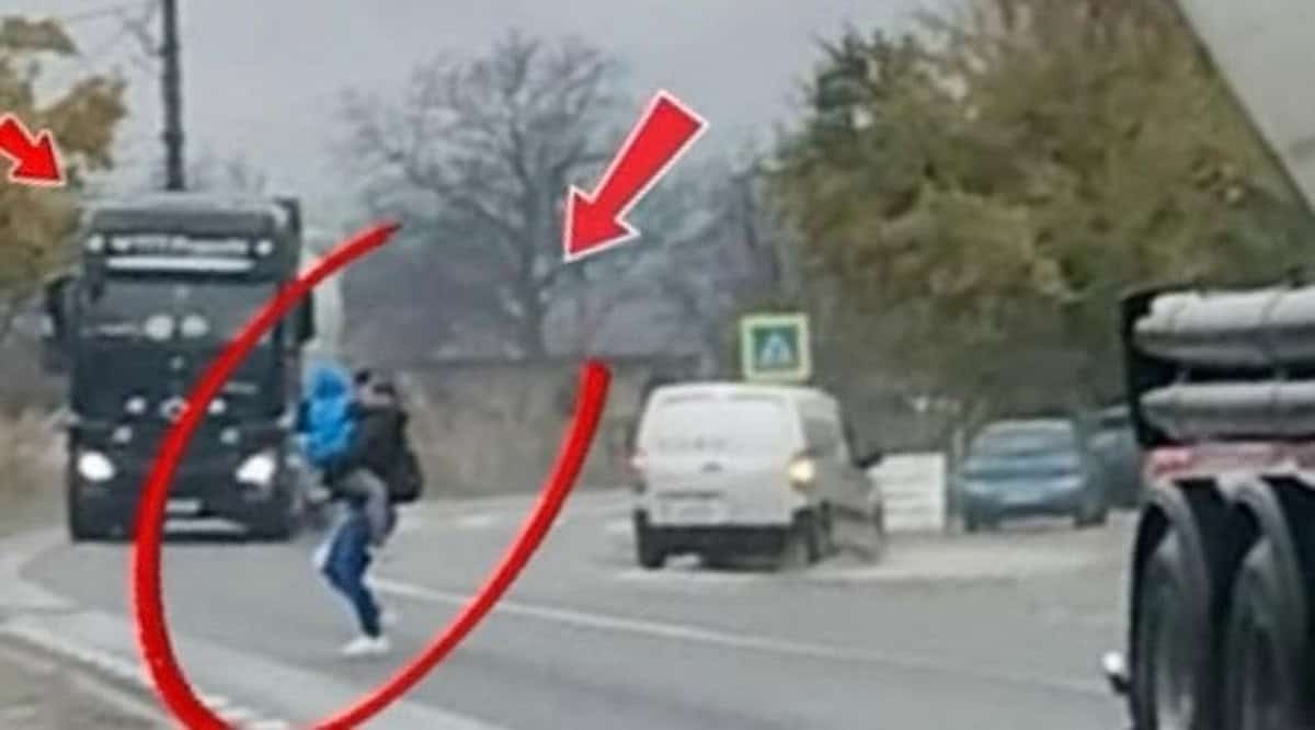 Mamă cu copilul în brațe traversează strada printre autocamioane ignorând siguranța pietonilor