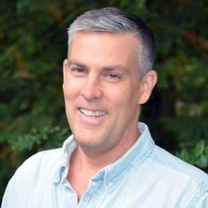 Smiling man in a blue shirt in front of trees