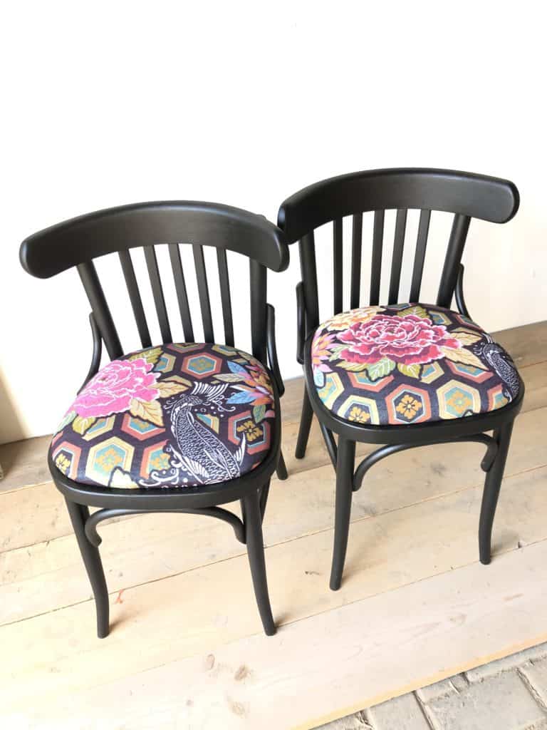 Elegante zwarte stoelen met kleurrijke, vintage bloembekleding, perfect voor een stijlvol interieur.