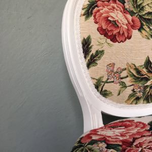 Antieke stoel met bloemenprint in pastelkleuren en witte houten lijst.