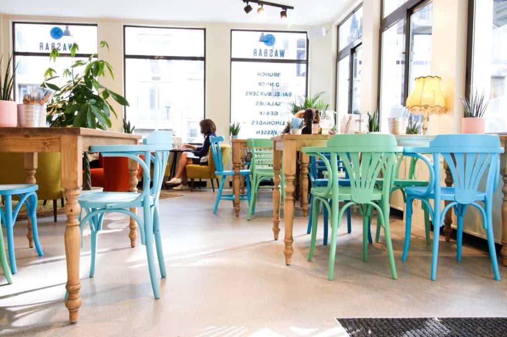 Gezellig koffiehuis met kleurrijke stoelen en groene planten voor een uitnodigende sfeer.