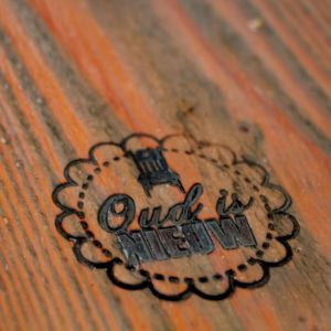 Oud is Nieuw logo geëtst op een houten tafel, benadrukt vakmanschap en authenticiteit voor een unieke sfeer.