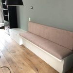 Alt tekst: Moderne wandbank met zachtgekleurde bekleding en witte houten basis in een woonkamer.