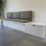 Eenvoudige en strakke houten bank met opbergruimte en comfortabele kussens, perfect voor moderne inrichtingen.
