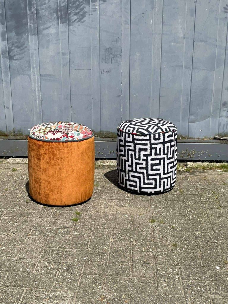 Alt: Twee kleurrijke, moderne poefs met oude en nieuwe stijlen buiten tegen een metalen muur.