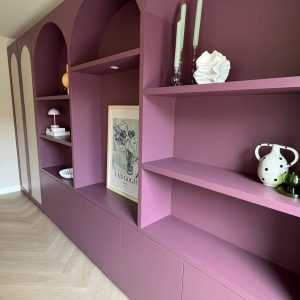 Alt: Modulaire boekenkast in paars tinten met decoratieve accessoires en kunstwerk.