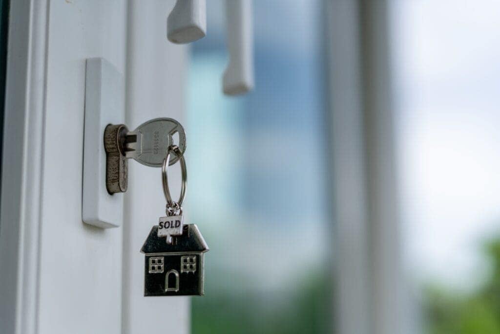 Modern house key with "SOLD" house-shaped keychain hanging on a white door lock.