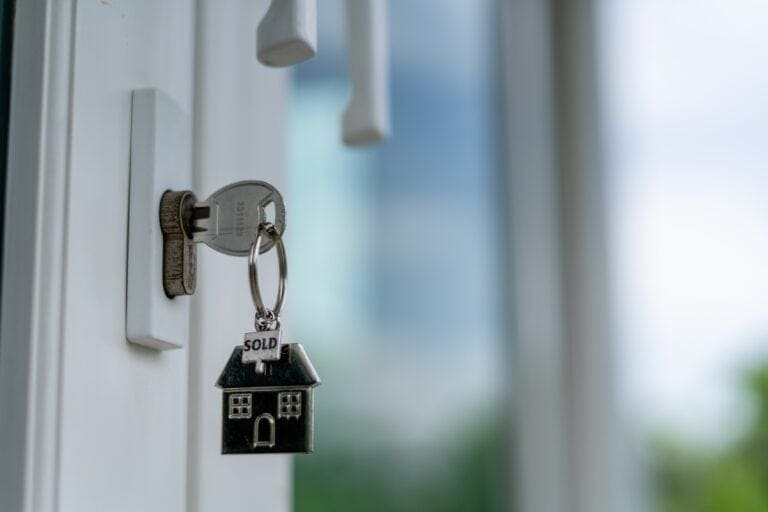 Modern house key with "SOLD" house-shaped keychain hanging on a white door lock.