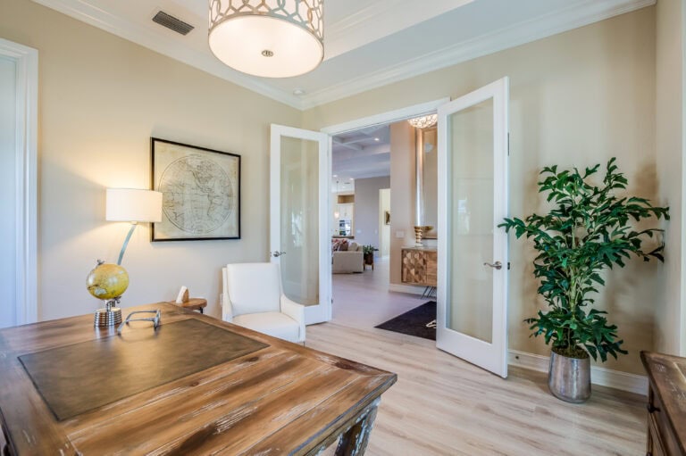 Bright and inviting home interior featuring open double doors, a wooden dining table, a white chair, a potted plant, and soft lighting, showcasing a stylish and comfortable living space.
